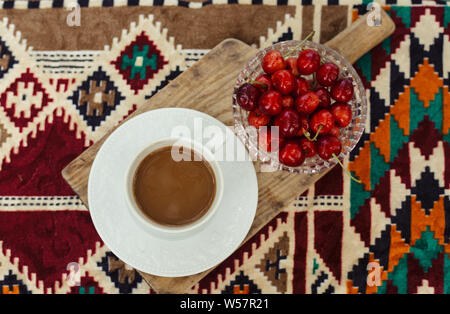 Tazza di caffè e le ciliegie sul manto colorato Foto Stock