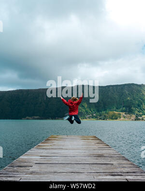 Giovane donna salta sul pontile di un lago Foto Stock