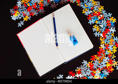 Libro bianco con matita e temperamatite accanto a pezzi di un puzzle. Foto Stock