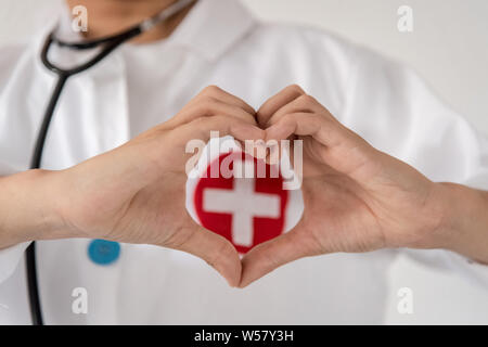 Bambino cuore con le mani in un dottore uniforme con il simbolo della croce rossa. Close up di giovani ragazzi dita fare l'amore concetto di salute. Foto Stock