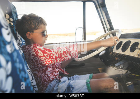 Bel ragazzo adolescente con occhiali da sole in posa affascinante alla guida di una annata van vestito come un fiore bambino hippie. Concetto di libertà e illuminante holid Foto Stock