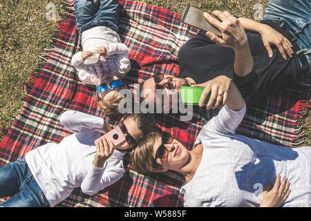 Giovane famiglia felice gioca selfies con telefoni cellulari. mamma e papà due piccole figlie scherzo divertito con occhiali da sole e chattare tra di loro. concetto o Foto Stock