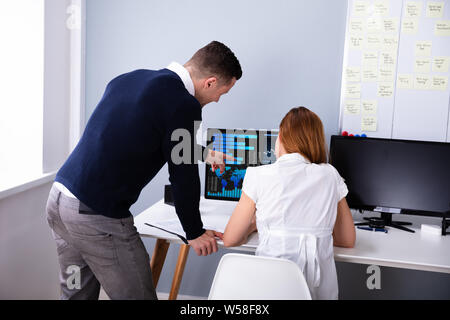 Vista posteriore di due imprenditori analizzando il grafico su schermo di computer in ufficio Foto Stock