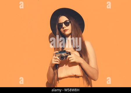 Giovane ragazza hipster con un vintage foto fotocamera e alla moda da indossare occhiali da sole e un cappello nero Foto Stock