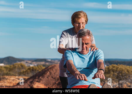 Senior donna aiutano gli anziani uomo mentre facendo un esercizio di stiramento all aperto con cielo blu sullo sfondo Foto Stock