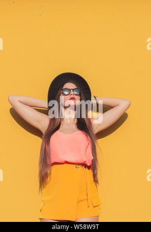 Giovane ragazza guardando il sole indossando un quartiere alla moda di occhiali da sole e un cappello nero Foto Stock