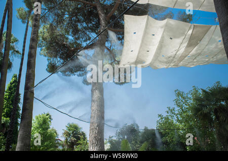 Tenda gli sprinkler e gli spruzzi di acqua nebulizzata a parco pubblico. Dispositivi per il raffreddamento della calda estate la temperatura in Spagna all'aperto Foto Stock