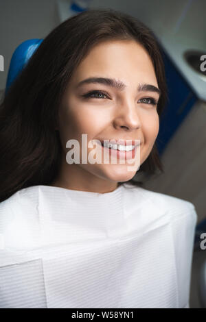 Felice giovane donna paziente sdraiato sulla poltrona odontoiatrica sotto la lampada medico in clinica Foto Stock