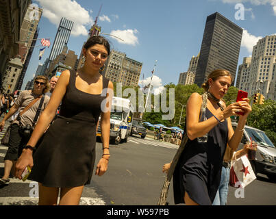 Distratti millennial, immersi in uno smartphone, cross West 23rd Street a New York il giovedì, 25 luglio 2019. (© Richard B. Levine) Foto Stock