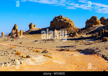 Marrone rossiccio strada sterrata che conduce verso il deserto formazioni rocciose nella luce del sole di mattina sotto cieli azzurri. Foto Stock