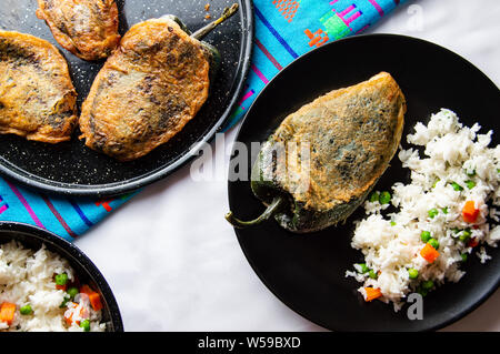 Mexican peperoncini ripieni (Chiles Rellenos), peperoncino poblano ripieni di formaggio e rivestito con una pastella di luce. Servito con riso e salsa di pomodoro rosso Foto Stock