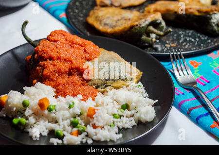 Mexican peperoncini ripieni (Chiles Rellenos), peperoncino poblano ripieni di formaggio e rivestito con una pastella di luce. Servito con riso e salsa di pomodoro rosso Foto Stock