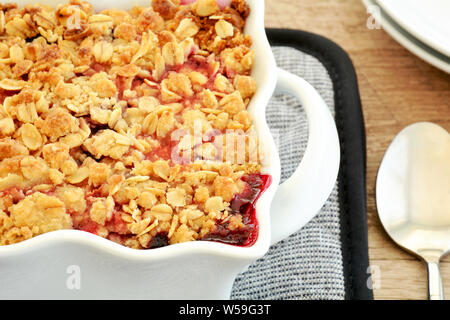 Primo piano della sfornato fresco Lampone Mirtillo crumble per due in bianco piccola casseruola in formato orizzontale. Deliziosi piatti di stagione freschi dessert di frutti di bosco Foto Stock