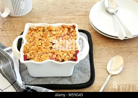 Sfornato fresco Lampone Mirtillo crumble per due in bianco piccola casseruola in formato verticale. Deliziosi piatti di stagione freschi dessert berry. Foto Stock