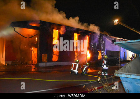 Rosengarten, Germania. 26 Luglio, 2019. Una casa residenziale e una falegnameria sono sul fuoco in Karl-Kurz-Straße in Rosengarten-Uttenhofen, vigili del fuoco tenere acqua di spegnimento in fiamme. Un grave incendio nel Rosengarten (Schwäbisch Hall quartiere) ha provocato un danno di un milione di euro. Secondo la polizia, una società di costruzione era andato in fiamme il venerdì sera. Quindi la propagazione di un incendio in una casa. Credito: Marvin Koss/onw-immagini.de via rete Ostalb/dpa/Alamy Live News Foto Stock