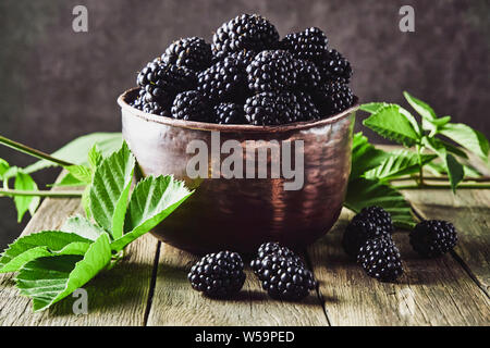 More mature con foglie in vecchi piatti di rame su vecchie tavole di legno e che giace accanto a un cucchiaio su uno sfondo scuro. Foto Stock