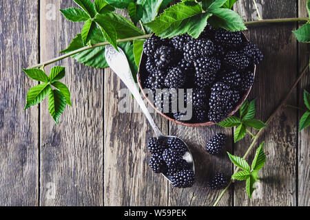 More mature con foglie in vecchi piatti di rame su vecchie tavole di legno e che giace accanto a un cucchiaio su uno sfondo scuro. Foto Stock