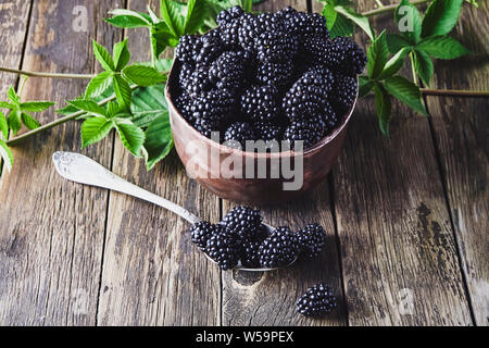 More mature con foglie in vecchi piatti di rame su vecchie tavole di legno e che giace accanto a un cucchiaio su uno sfondo scuro. Foto Stock