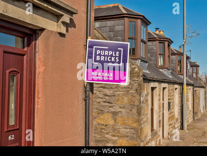 Mattoni di colore viola in vendita segno di una strada con case e il segno sul muro di una casa Foto Stock