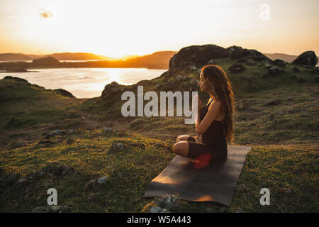 Donna fare yoga da soli ad alba con la montagna e vista oceano. Armonia con la natura. Auto-analisi e anima-ricerca Foto Stock