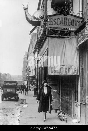 Uno dei primi anni del ventesimo secolo in bianco e nero fotografia scattata a Parigi, Francia. La foto mostra una donna camminare davanti a un ristorante di lumaca o Escargots ristorante. Un modello di grandi dimensioni di una lumaca si trova sopra il ristorante. Foto Stock