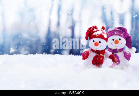 Due piccoli pupazzi di neve la ragazza e il ragazzo in cappelli e sciarpe sulla neve in inverno. Sfondo di festa con un divertente pupazzo di neve. Scheda di Natale, copia dello spazio. Foto Stock