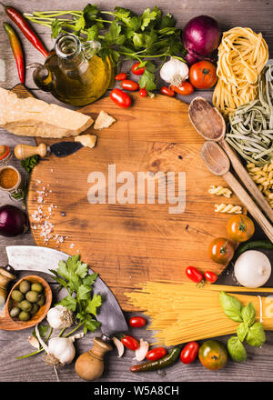 Disposto sul tagliere di legno di vari tipi di verdure ed erbe aromatiche con olio d'oliva e parmigiano a cucinare alcuni tipi di pasta italiana Foto Stock