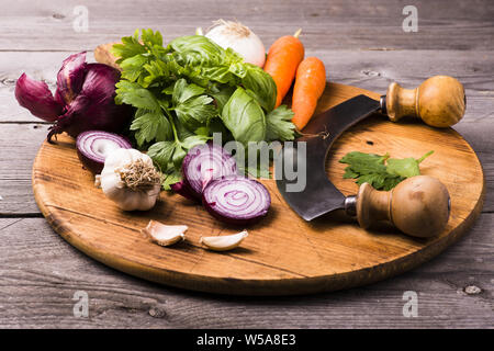 Verdure fresche ed erbe in primo piano disposto sul tagliere di legno pronto per tritare con la mezzaluna. Foto Stock