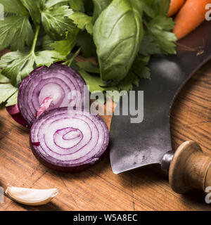 Verdure fresche ed erbe in primo piano disposto sul tagliere di legno pronto per tritare con la mezzaluna. Foto Stock