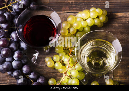 Su tavola in legno rustico di bicchieri di vino bianco e rosso con uve miste Foto Stock