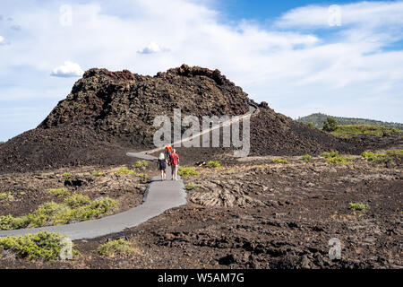 Arco, Idaho - Giugno 30, 2019: gli escursionisti a piedi fino la conetti eruttivi trail, un passaggio pedonale lastricata che conduce a un cono di scorie wi nei crateri della luna Monum nazionale Foto Stock