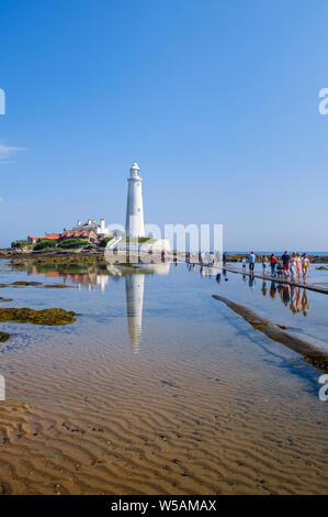 Il Northumberland coast - trippers giorno i turisti e le famiglie a piedi attraversata la strada rialzata a St Mary's Faro a Whitley Bay North Tyneside Foto Stock