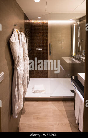 Un rinnovato di recente il bagno in un albergo di lusso con una passeggiata nella doccia e accappatoi in una luminosa stanza Foto Stock