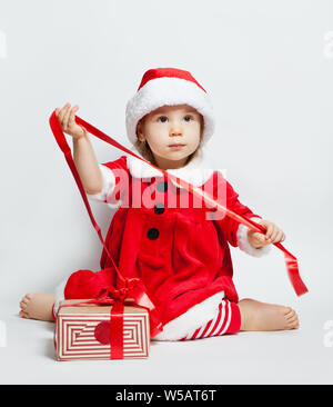 Natale bambino in Santa hat apertura confezione regalo rossa su bianco con verde albero di Natale ramoscello e nuovo anno decorazione Foto Stock