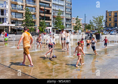 Adulti e bambini a giocare in acqua di fontana per rinfrescarsi nelle temperature di brucianti durante l'ondata di caldo in estate Foto Stock
