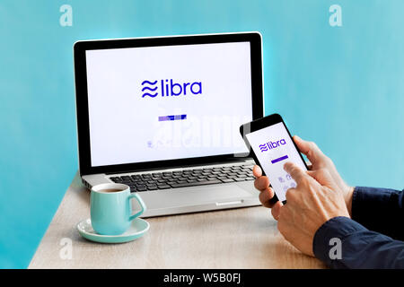 Maschio caucasico mano utilizzando Facebook Libra Crypto valuta digitale App su smartphone e computer portatile Foto Stock