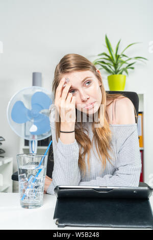 Una giovane donna in ufficio raffredda la sua fronte con un cubetto di ghiaccio Foto Stock