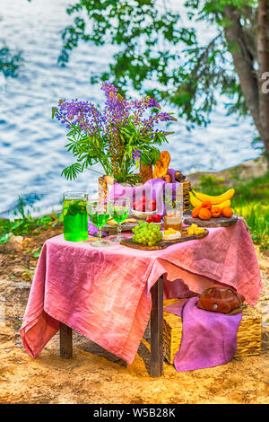 Pic-nic nei pressi acqua al tavolo con fiori in frutti di bosco e verdure Foto Stock