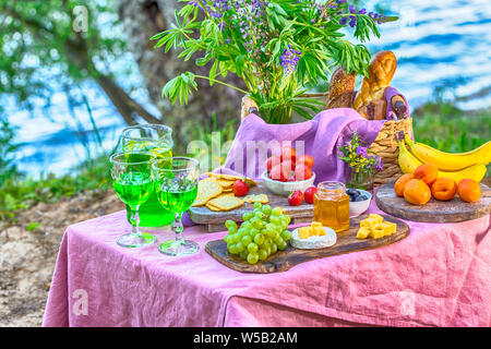 Pic-nic nei pressi acqua al tavolo con fiori in frutti di bosco e verdure Foto Stock