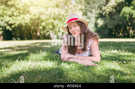 Donna ritratto all'aperto. Felice, giovane donna posa su erba verde, in estate park. Foto Stock