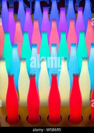File di bottiglie allineate come una parte di un gioco di carnevale sono illuminati in luminosi colori al neon. Foto Stock