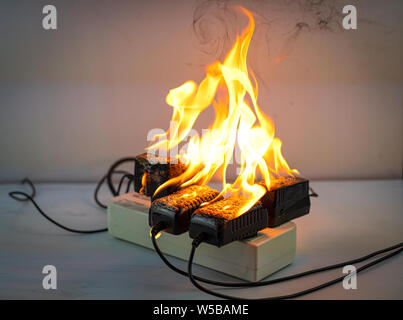 Sul fuoco un adattatore a spina femmina su sfondo bianco, corto circuito elettrico a guasto derivante in elettricità filo bruciato Foto Stock