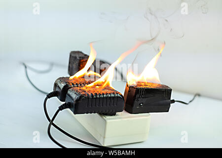 Sul fuoco un adattatore a spina femmina su sfondo bianco, corto circuito elettrico a guasto derivante in elettricità filo bruciato Foto Stock