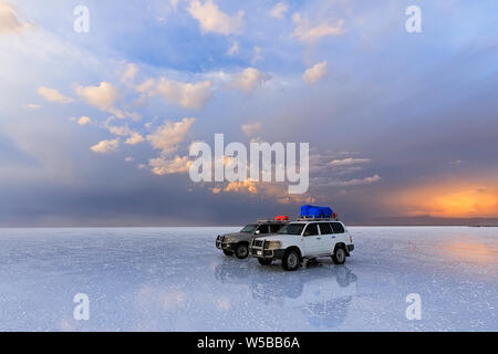 Due veicoli fuoristrada stand sulla distesa di sale di Uyunu al tramonto da favola - Altiplano, Sud America. Foto Stock