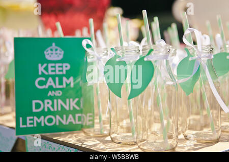 Primo piano di molte bottiglie vuote per la limonata o un cocktail con una paglia a strisce e una foglia verde decor e un cartello che diceva di mantenere la calma e di bere la limonata, s Foto Stock