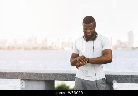 Nero sportivo guy controllando la frequenza cardiaca su smartwatch e sorridente Foto Stock