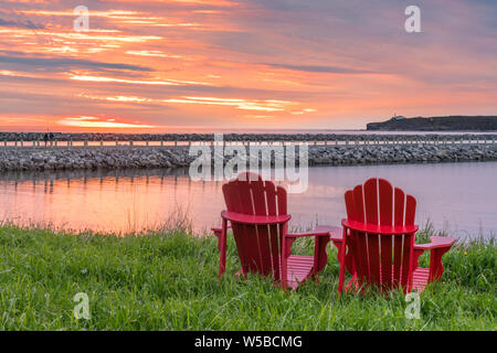 Rosso sedie adirondack lungo l'oceano durante il tramonto di Rocky Harbour, Terranova, Canada Foto Stock