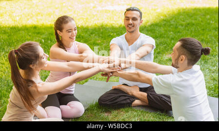 Quattro amici mettendo insieme le mani dopo aver superato con successo la pratica dello yoga Foto Stock