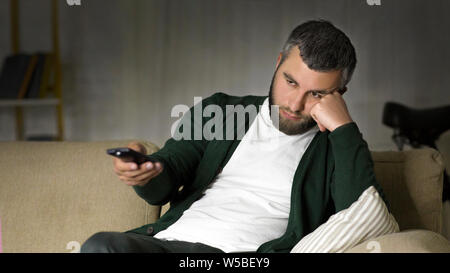Annoiato uomo canali di commutazione sulla TV di casa Foto Stock