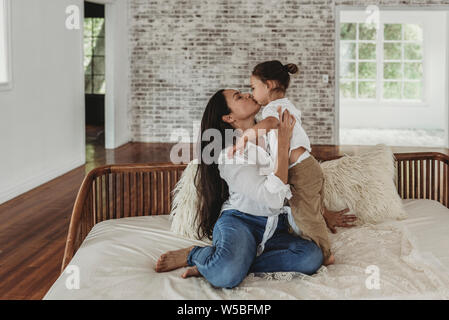 Giovane madre baciare toddler boy sul lettino di luce naturale e in studio Foto Stock